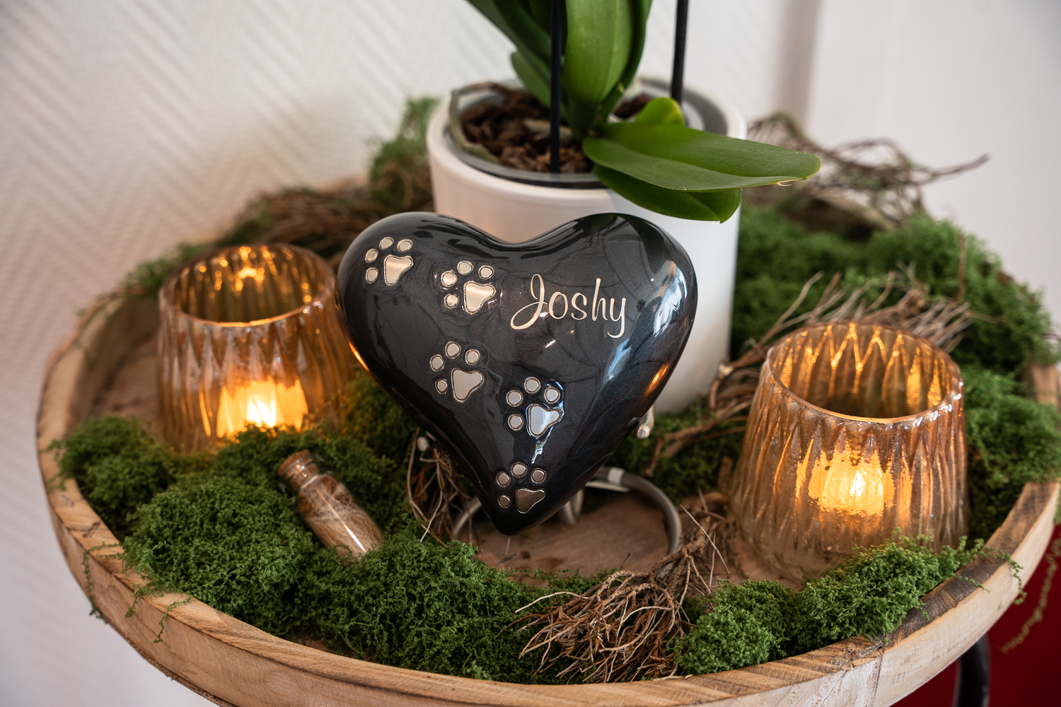 Eine Urne steht auf einem Tisch. Von Moos umrandet und mit zwei leuchtenden Kerzen